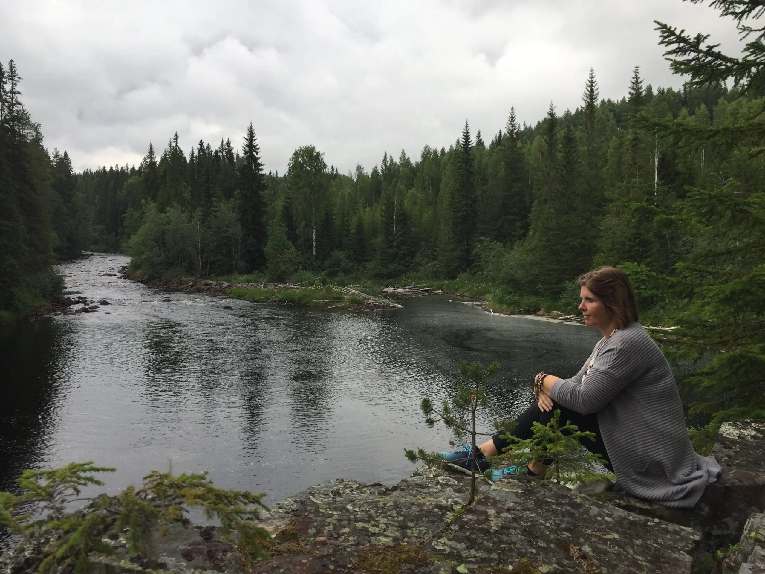 Manja sidder ved en flod i skoven og nyder naturens ro.