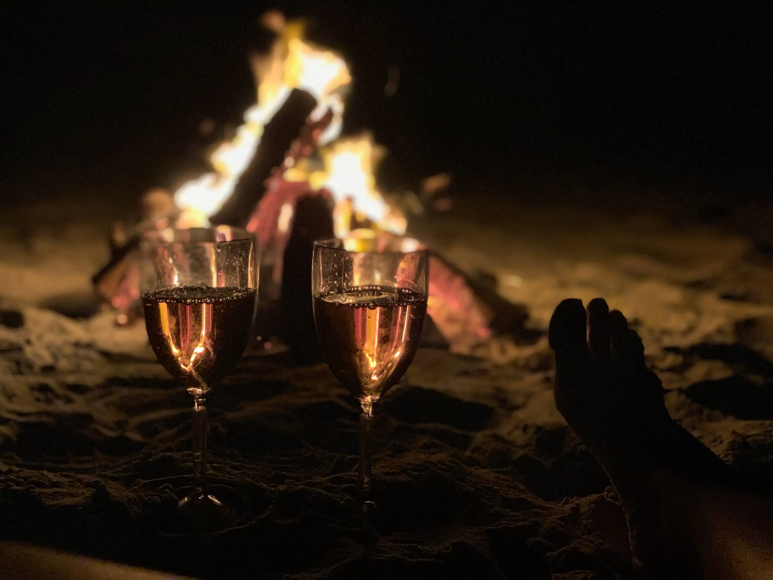 To glas vin foran et bål på stranden om aftenen.