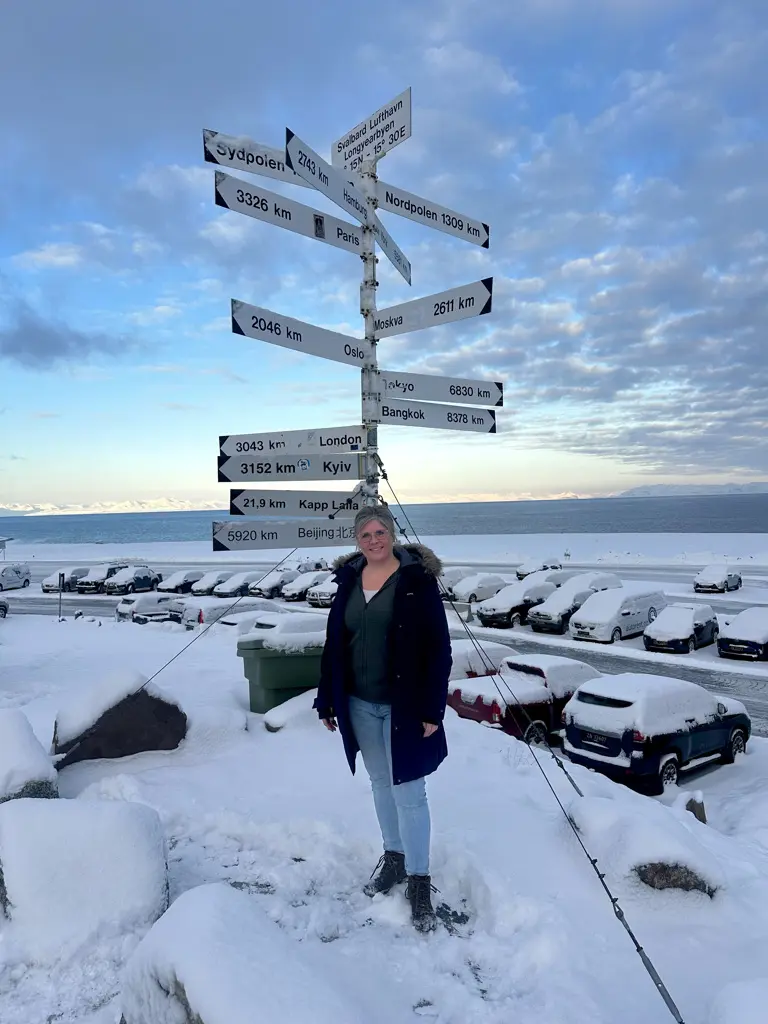 Manja foran et verdensskilt i det sneklædte Svalbard ved siden af lufthavnen.