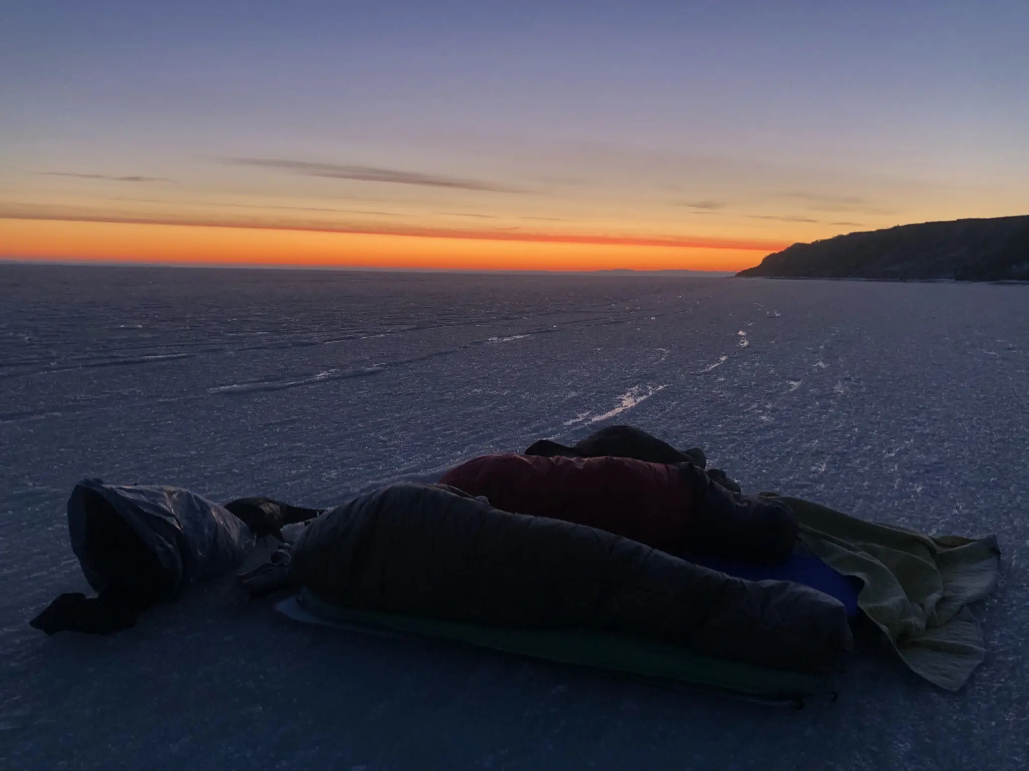 Person i sovepose på isen under en smuk solnedgang ved Hvisker med heste.