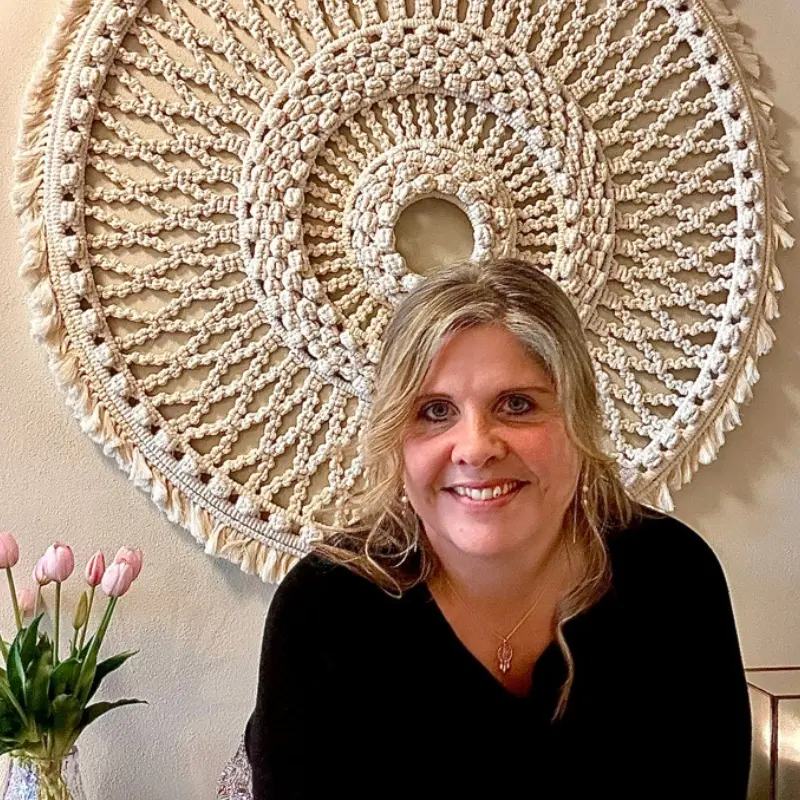 Smilende kvinde foran macrame vaegelement paa kontaktsiden for Hvisker med Heste.